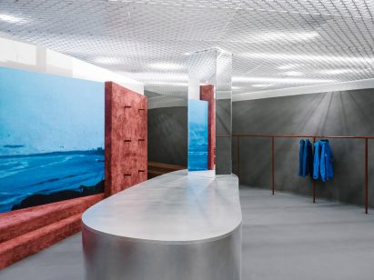 Shop interior with grey floor, silver island and rammed-earth steps and partition wall