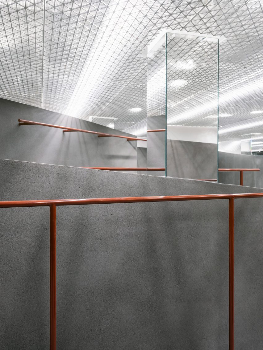 Grey wall of a shop into with a mirror and orange clothes rail