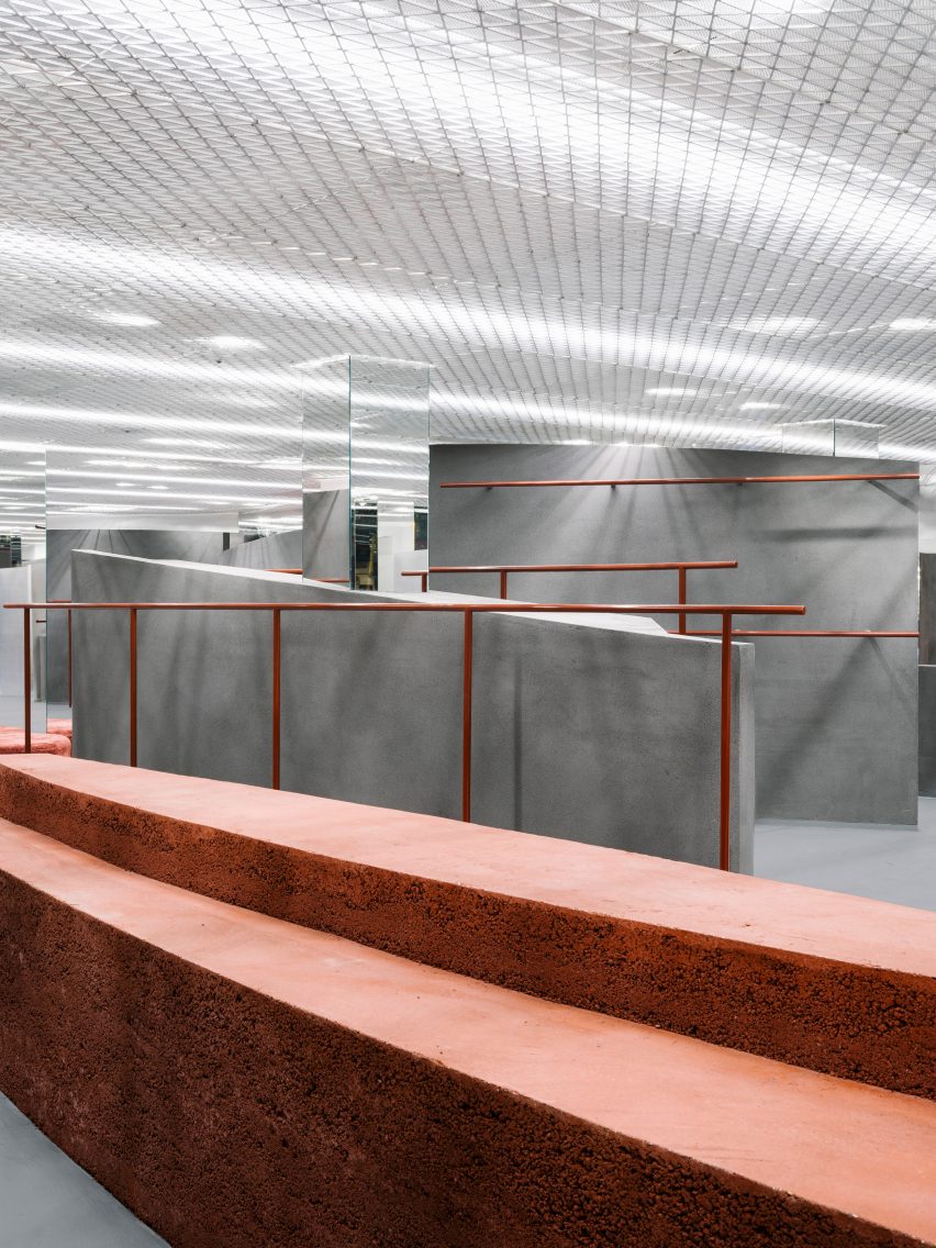 Shop interior with curved grey walls, orange clothes rails and rammed-earth island