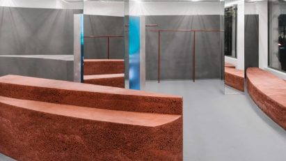 Shop front with stone facade and large window looking into a store with rammed-earth islands