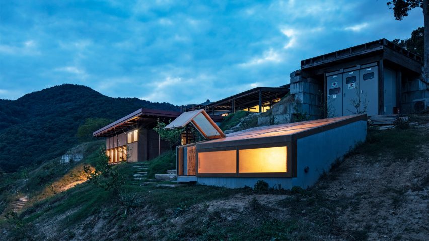 Concrete bunker building with a translucent sloped roof on a hillside with other buildings in the distance