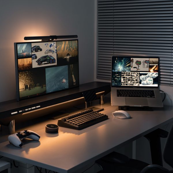 Photo of a desktop with a monitor, laptop and accessories supported on the Hexcal Studio desktop management system, lit by the soft glow of an indirect light