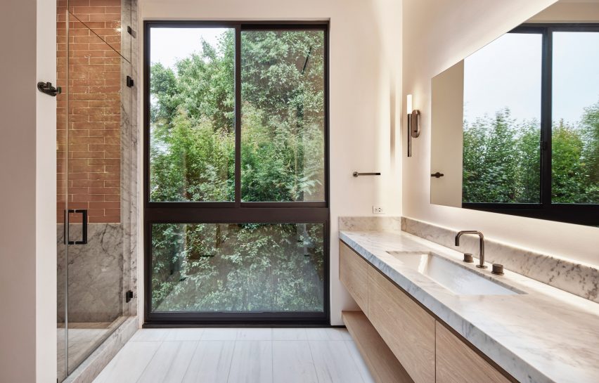 White bathroom with marble countertop and large window overlooking a garden