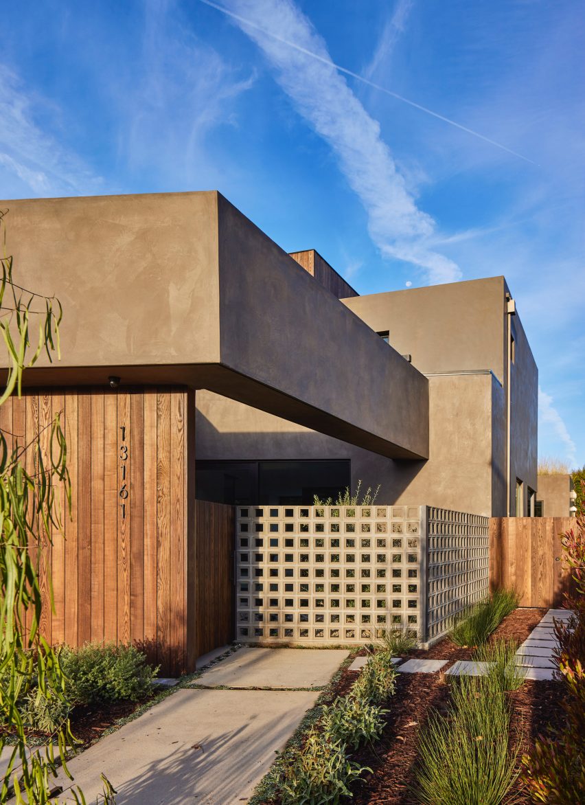 Side entrance of a stucco and ash-clad home with planted garden patches