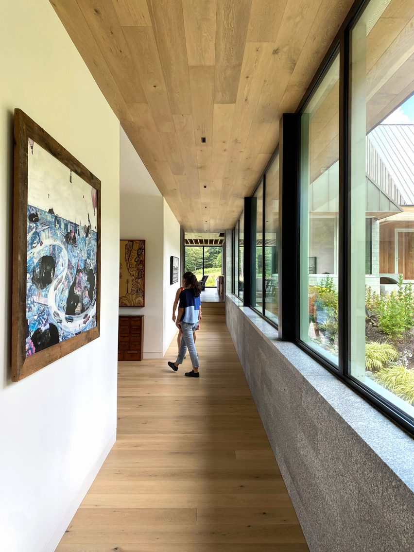 A corridor with wood flooring and ceiling, a white internal wall on one side and a concrete exterior wall with windows