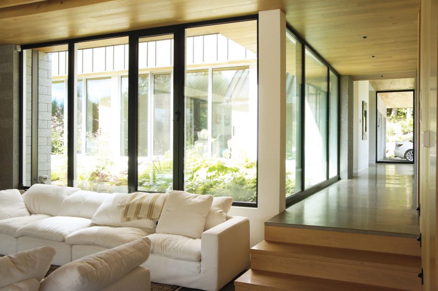 Two timber steps leading down to a living room with a white sofa and large windows overlooking a courtyard