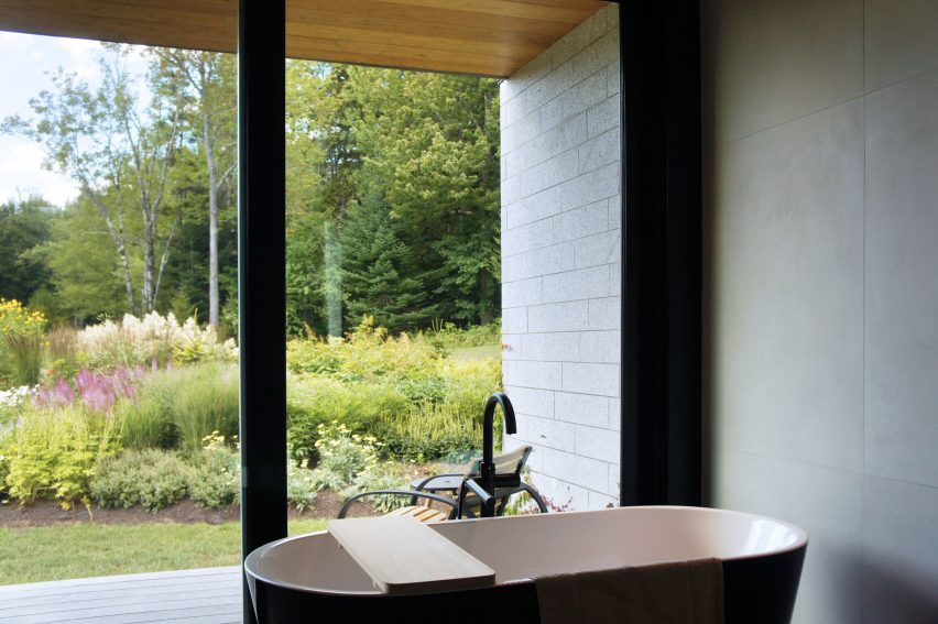 A bathroom with a freestanding bathtub and floor-to-ceiling windows overlooking a planted garden