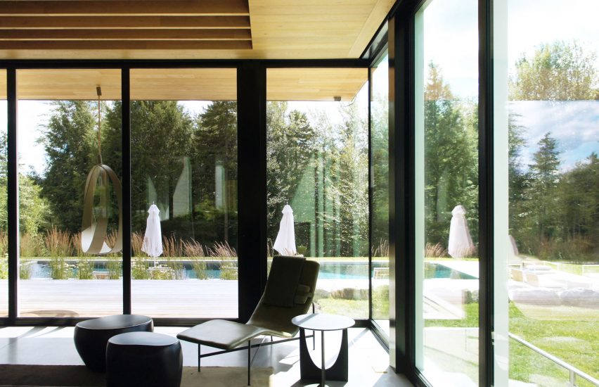 A corner on a lounge space with a chair next to floor-to-ceiling windows overlooking a garden