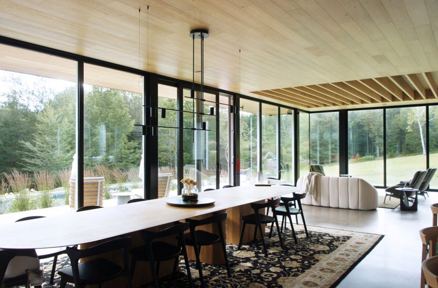 An open-plan living and dining room with a long wooden table and floor-to-ceiling windows