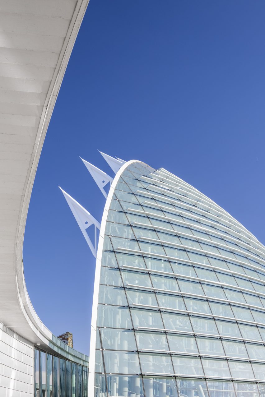 A tall arched building with glass facade and metal fins extending from the back