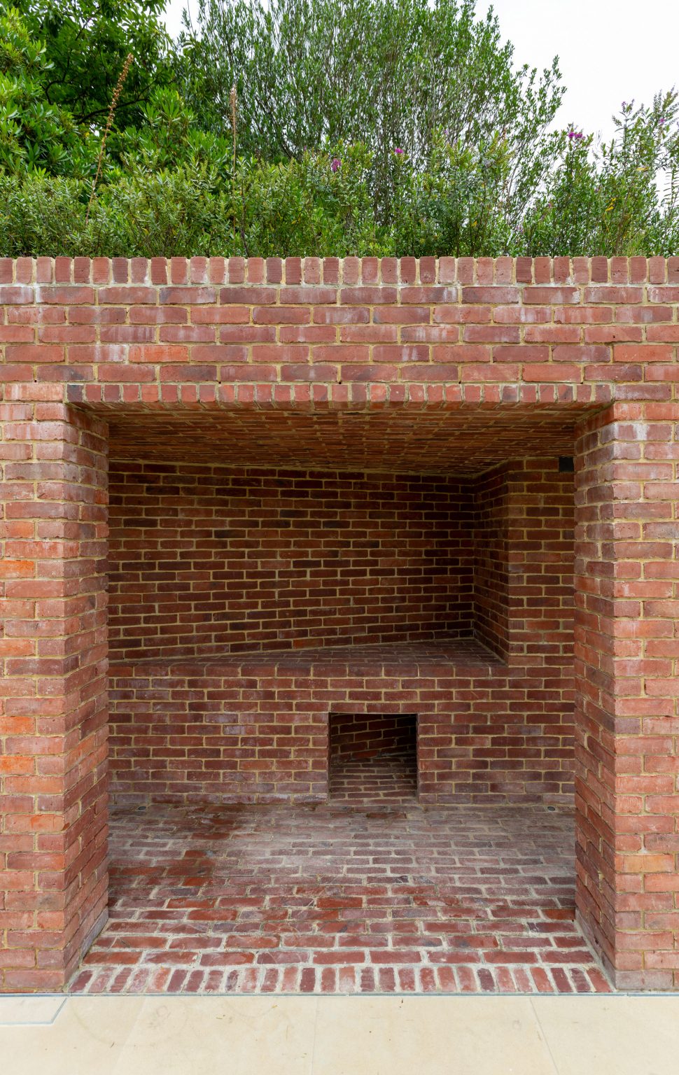 Brick structure with a square opening leading to a brick bench and planting on the roof