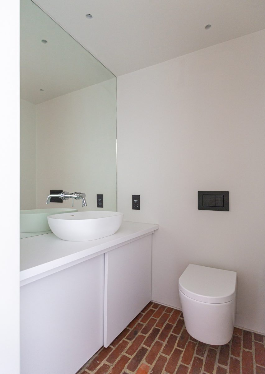White bathroom with counter-top sink, toilet and brick floor
