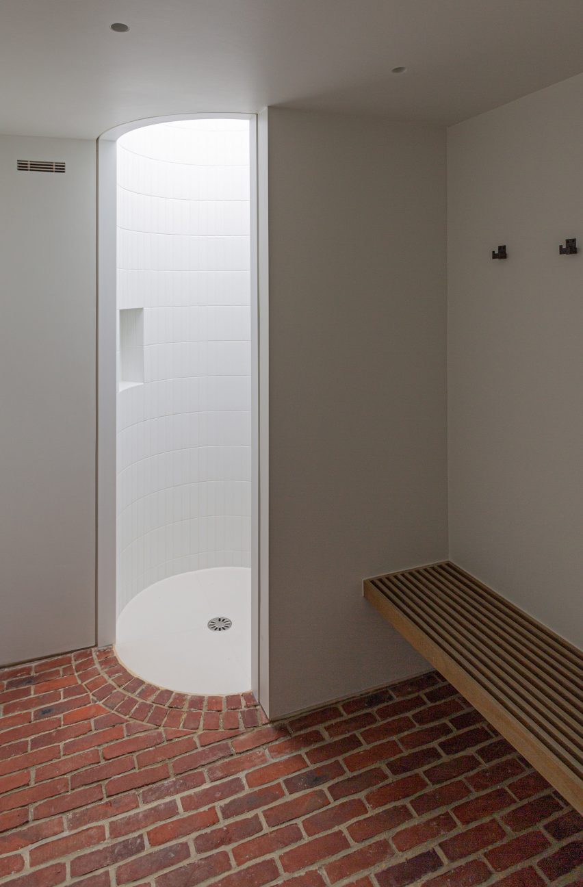 White bathroom with brick floor, circular shower and wood bench