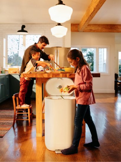 Photo of a girl sliding food scraps into the Mill bin in her family kitchen
