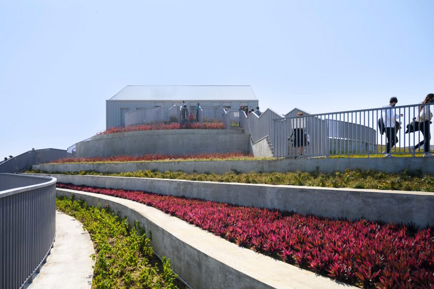 A series of stepped terraces filled with different coloured planting and a pitched-roof building