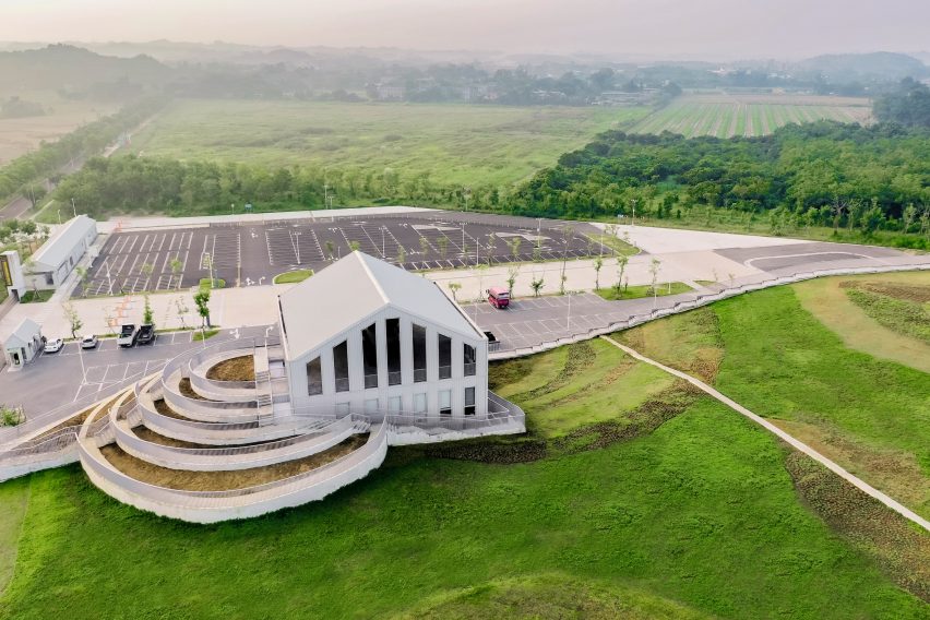 Curving grass roof, stepped terraces and a pitched-roof building surrounded by fields