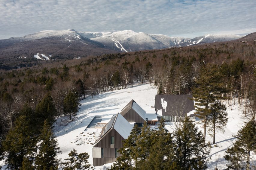 Three granite and metal cabins in a snowy clearing on a mountain surrounded by trees