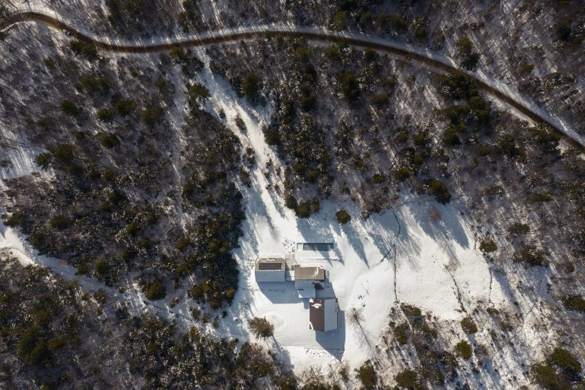 Aerial view of a home made up of three cabins in a snowy clearing in a forest