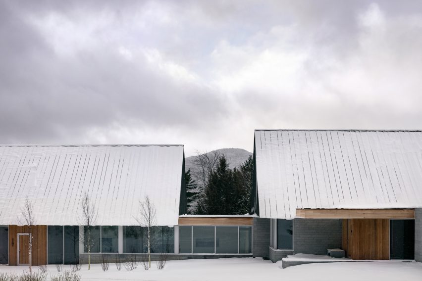 Two cabins with granite walls and metal roofs connected by a glazed walkway