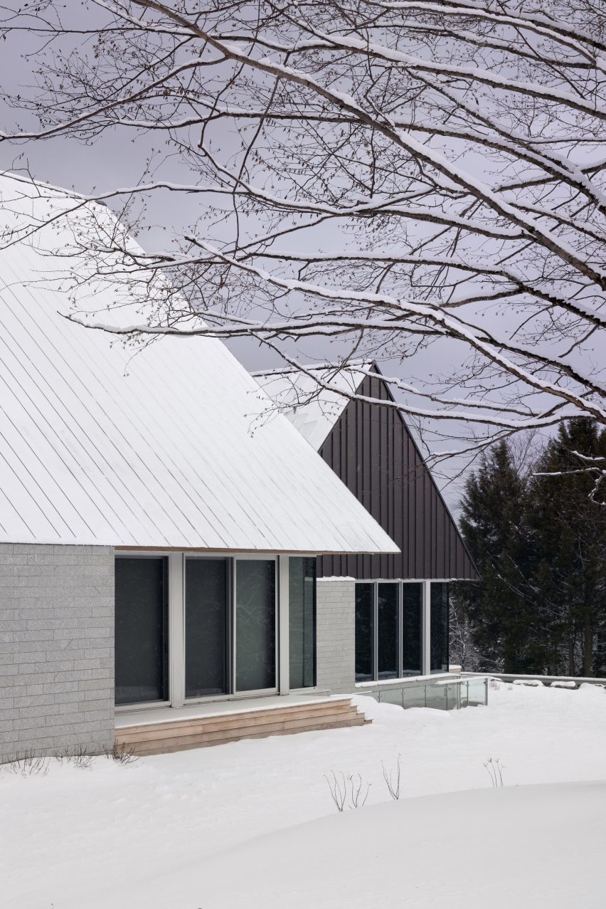 Two cabins with granite walls and metal roofs in a snowy clearing with trees
