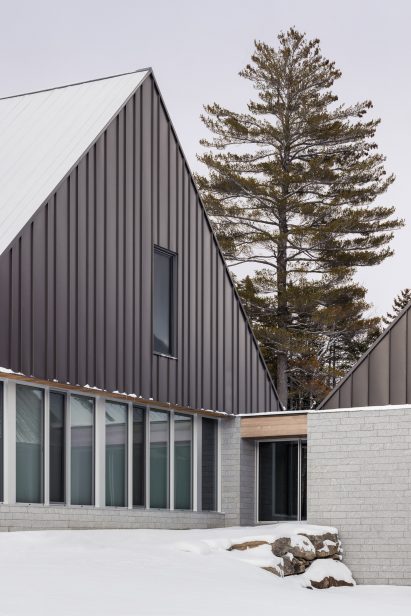 A pitched-roof cabin with granite walls and a metal-clad gable end on a snowy mountain