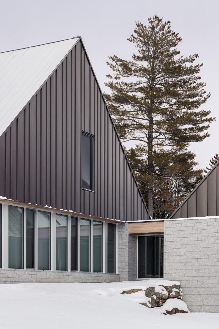A pitched-roof cabin with granite walls and a metal-clad gable end on a snowy mountain