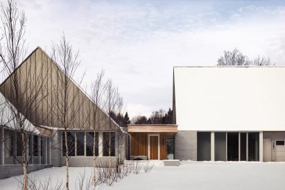 A series of pitched-roof structures with granite stone walls and metal-clad gable ends connected by timber-clad walkways on a snowy mountainside
