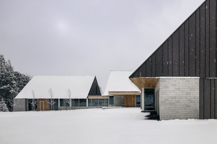 Three cabin structures with granite walls and metal-clad gable ends connected by glazed walkways on a snowy mountainside