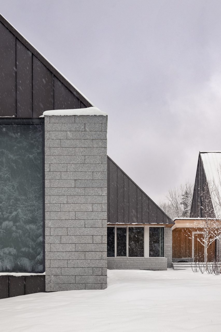 Three cabin structures with granite walls and metal-clad gable ends in a snowy clearing