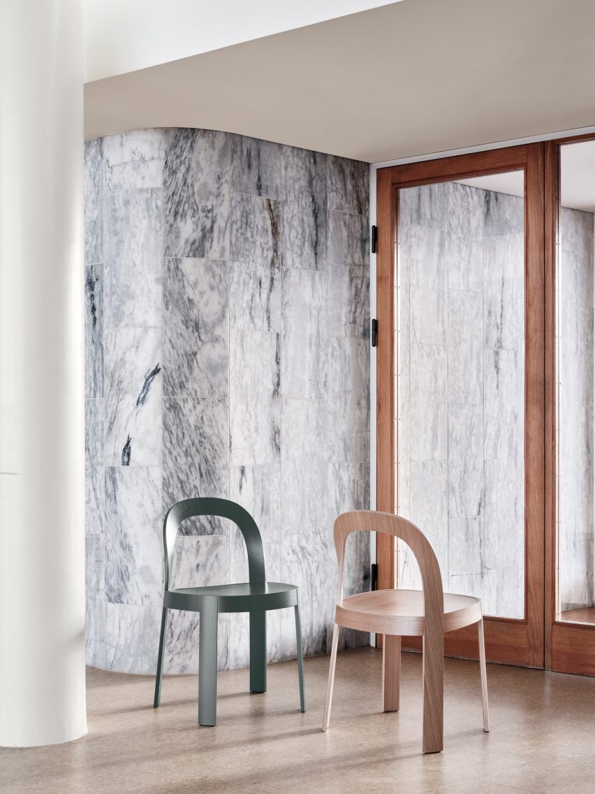 Two wooden chairs in front of stone-tiled interior wall
