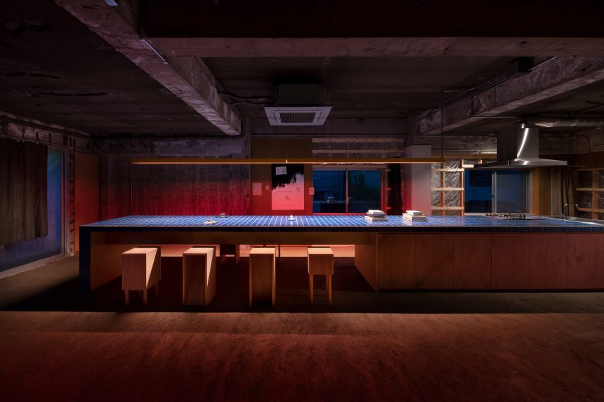 Long kitchen island bench topped with blue tiles in a dimly lit industrial apartment
