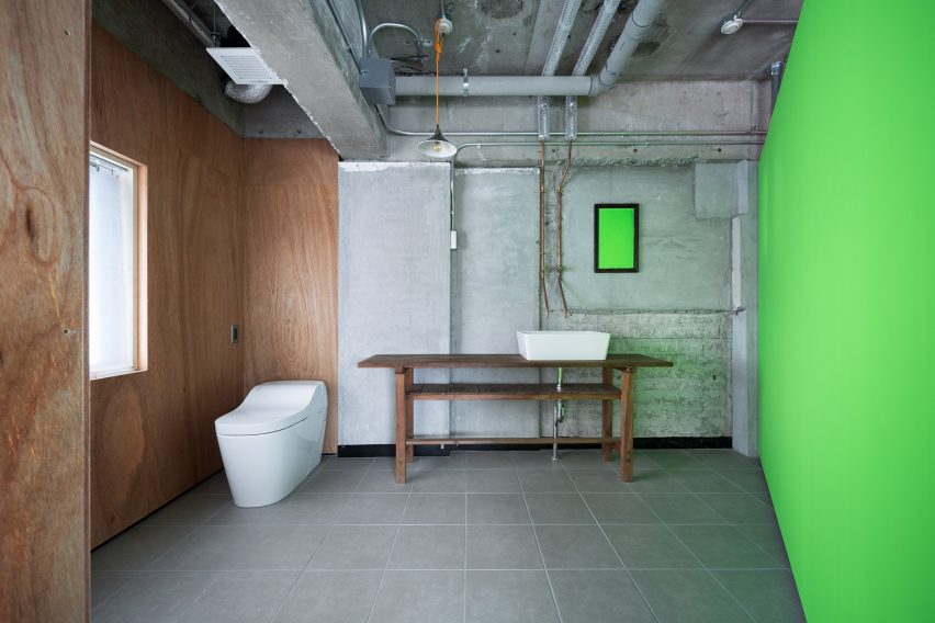 Toilet and sink on a wooden bench in an industrial bathroom with fluorescent green wall