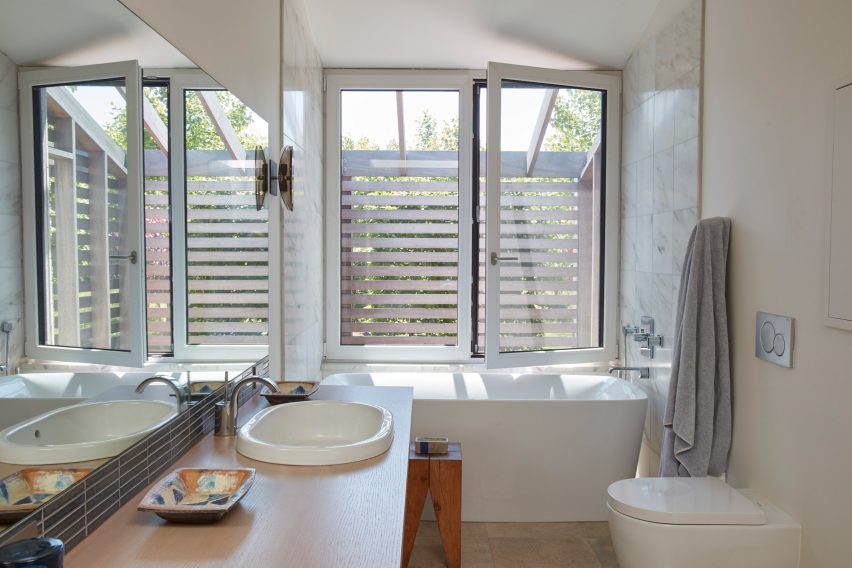 White bathroom with a large wall mirror, white basin and wood countertop