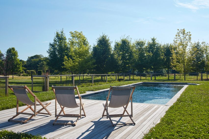 Outdoor swimming pool in a grassy garden with with timber decking and three deck chairs