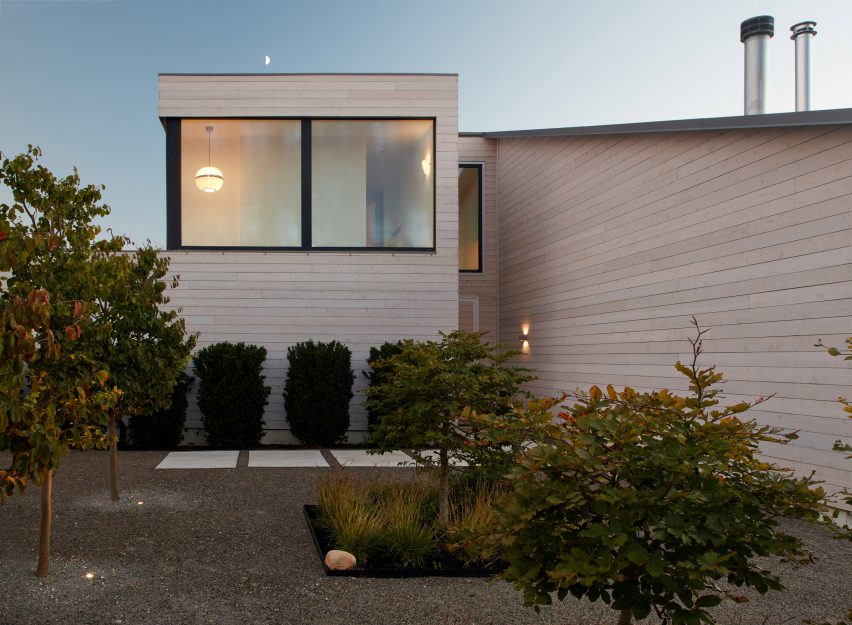 Two-storey cedar-clad home with large windows and gravel front garden with trees