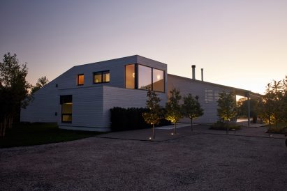 Exterior of a two-storey home with one-storey extensions clad in cedar and a gravel driveway