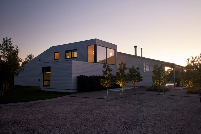 Exterior of a two-storey home with one-storey extensions clad in cedar and a gravel driveway