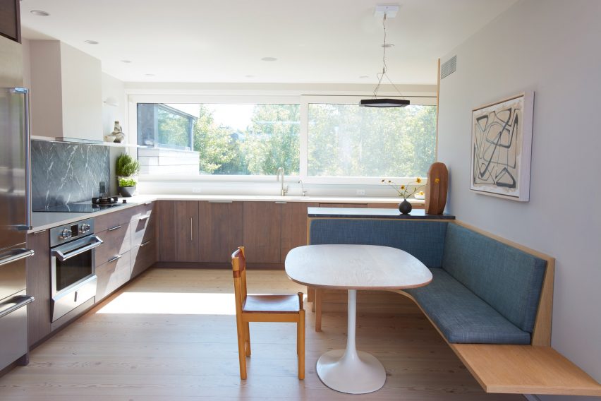 Interior of a kitchen with dark wood cabinets along two perpendicular walls and wooden bench seating by a white table