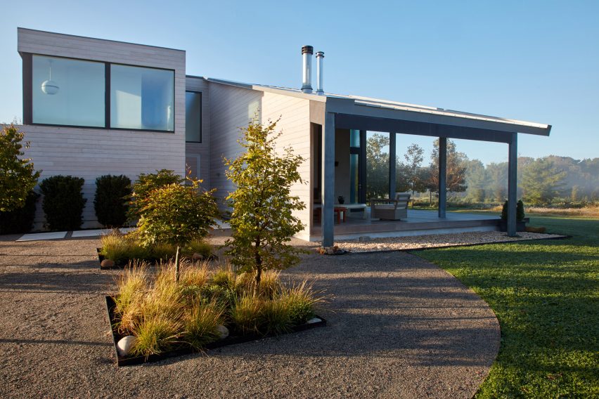 Two-storey cedar-clad home with a large porch, gravel driveway and grassy garden