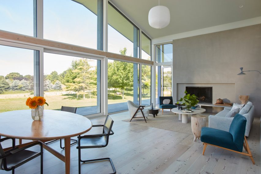 Interior double-height living space with white walls, glazed facade and wood floors, decorated with a circular table and lounge seating