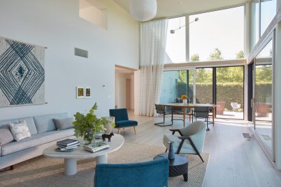 Double-height living room with a glazed elevation, white walls, and lounge chairs around a circular coffee table