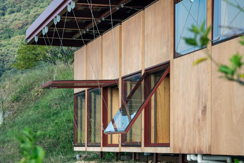 A wood-clad and red steel frame building with a series of large top-hinged windows opened at different degrees