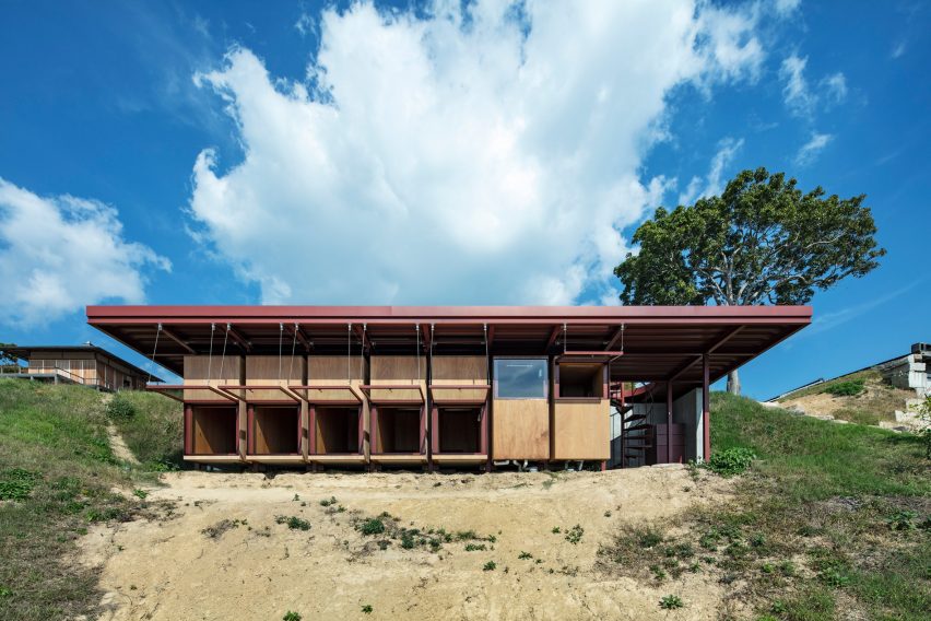 A guesthouse with large windows, wood walls and an overhanging red steel roof on a hillside