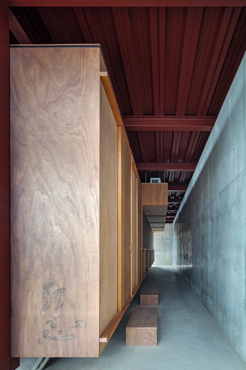 Concrete corridor with a red steel roof and wood boxes with sliding doors on one side