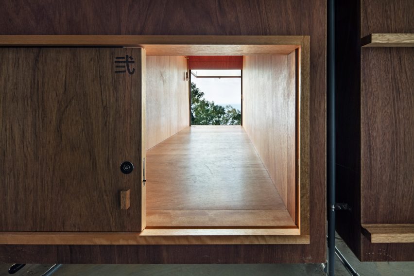 Sliding timber door leading to a wood-lined corridor with a window at the end overlooking treetops