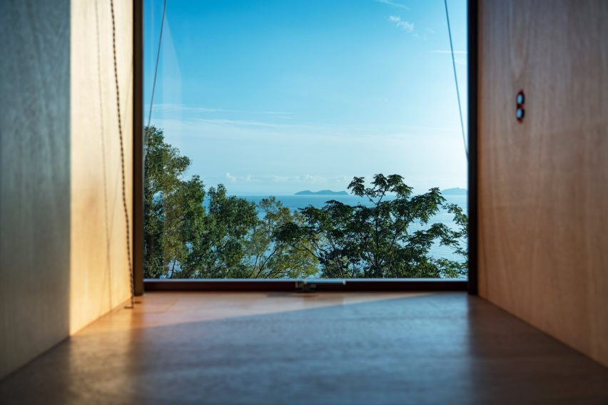 Interior room with timber floors and walls with a large window overlooking the sea and treetops