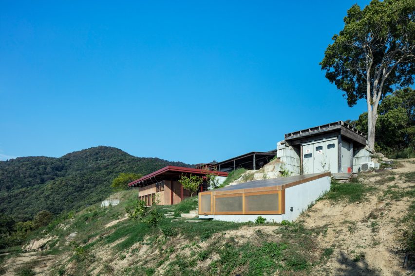 A bunker-style building is a sloped roof and a guesthouse with a red steel frame built into a hillside