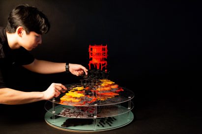 Photograph showing person adjusting multi-layered model on black backdrop
