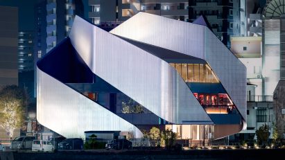 A theatre building on a city waterfront with sweeping steel panels covering the exterior