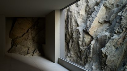 A dark empty room with floor-to-ceiling window looking onto rocky terrain